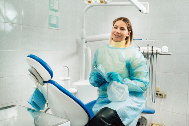 诊所一位戴着医用口罩和橡胶手套的女牙医坐在她的办公室里工具卫生健康