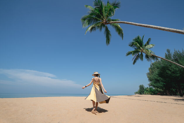 海洋走在椰子树下的女人 在沙滩上 天空湛蓝热带连衣裙温暖