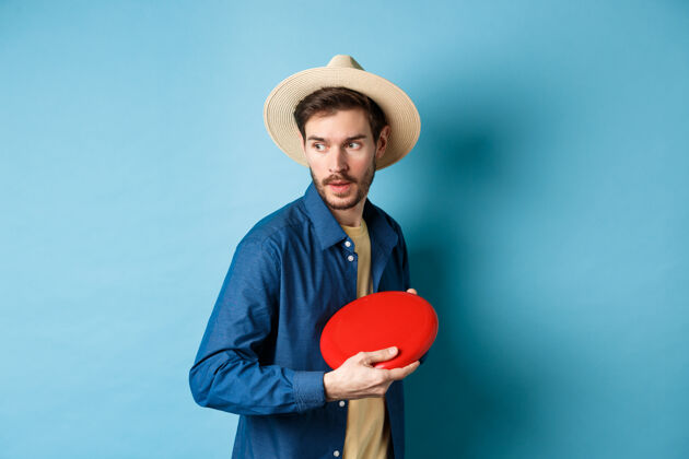 扔帅哥戴着夏天的帽子玩飞盘 把它扔到一边 站在蓝色的背景上胡子帽子人