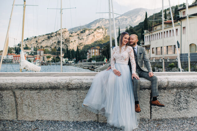 夏天意大利 加尔达湖一对美丽的夫妇在阿尔卑斯山脚下的意大利加尔达湖畔一男一女坐在意大利的码头上休闲男人生活方式