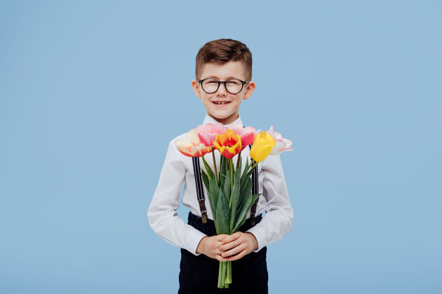 惊喜孩子微笑着戴着眼镜的小男孩你手上的花 隔离在蓝色的墙上快乐童年给予