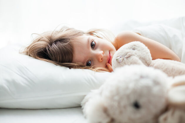毯子美丽的大眼睛小女孩躺在白色的床上 旁边放着兔子玩具女孩美丽舒适