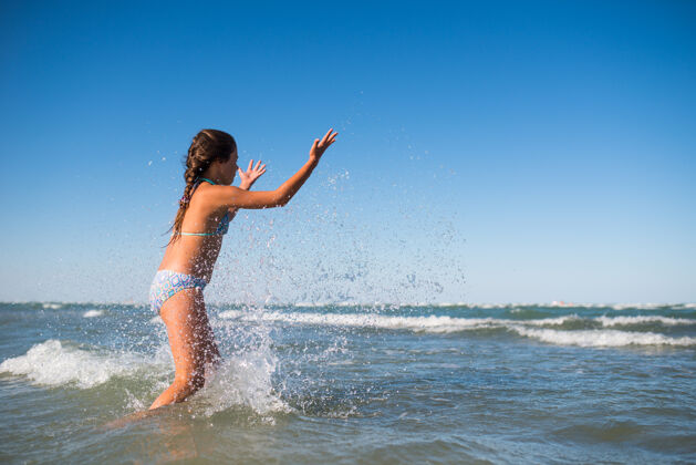 欢呼在一个阳光明媚温暖的夏日 活泼快乐的小女孩在喧闹的海浪中嬉戏玩耍年轻泡沫