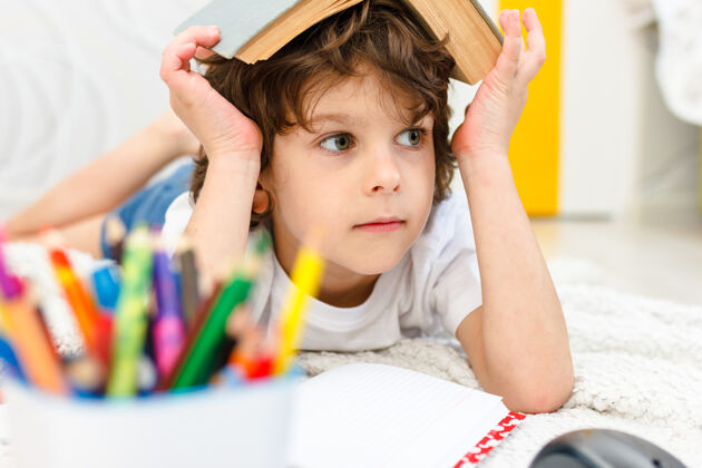 房间男孩在灯光室做作业 头上顶着一本书概念阅读 教育 童年隔离封锁中的社会距离和自我隔离学生男孩知识
