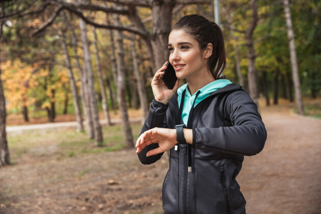 成人照片中 一位年轻漂亮的健身女士在公园里看手表 用手机聊天身体电话活跃
