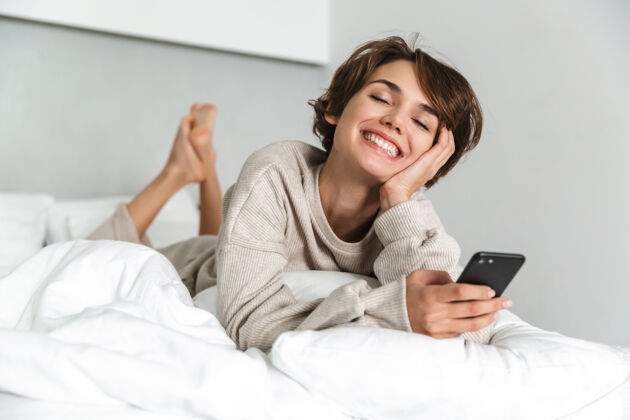 在线微笑的年轻女孩 早上在床上放松 用手机漂亮信息卧室