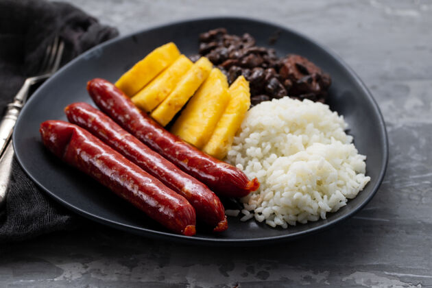 豆类香肠配米饭 黑豆和菠萝在深色盘子上羽衣甘蓝午餐热