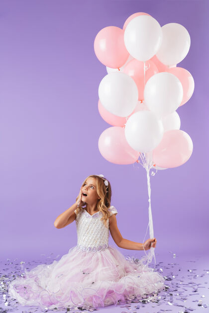 裙子穿着公主裙的漂亮小女孩孤立地坐在紫罗兰色的墙上 手里拿着一堆气球小快乐高加索