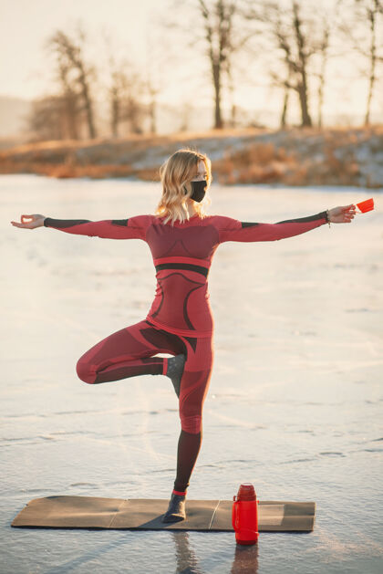 极端冬天 一个女孩在日落时在湖边的冰上做瑜伽女人运动瑜伽