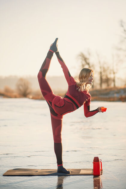 水晶冬天 一个女孩在日落时在湖边的冰上做瑜伽孤独姿势药