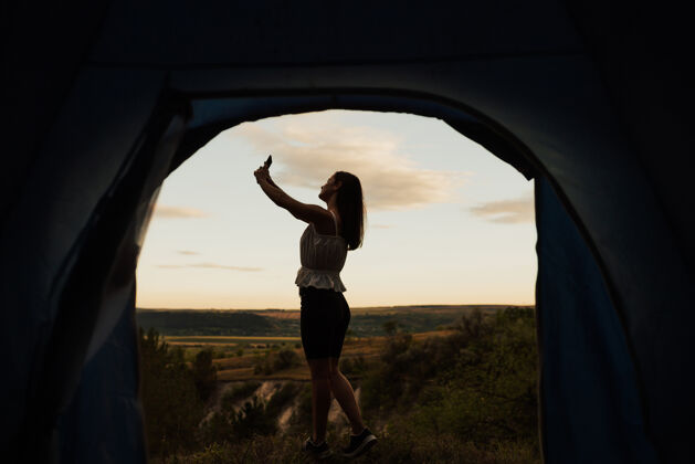 帐篷早上 美女拿着手机在一座山为背景的帐篷旁自拍环境休闲户外