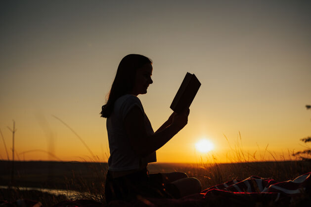 日落一个年轻女子在街上看书的剪影山她带着一本有趣的书在山上欣赏美丽的日落人冒险自然