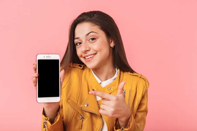 欢乐快乐的年轻女子孤零零地站在粉红色的墙上 展示着黑屏手机成人表情空白