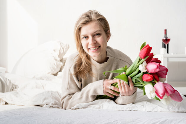 春天幸福的年轻女子穿着睡衣躺在床上捧着郁金香花束庆祝睡眠礼物