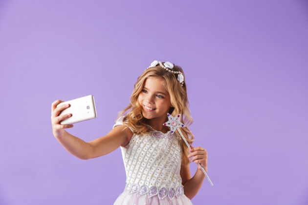 魔术一个微笑的可爱女孩的肖像 穿着公主裙 隔着紫罗兰色的墙 拿着魔杖 自拍自拍衣服小
