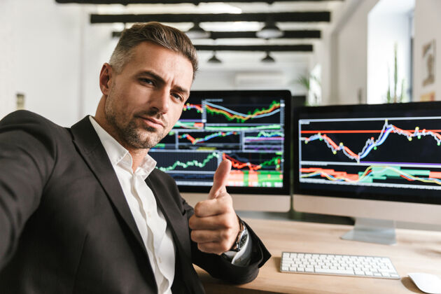 西装一张30多岁的自信男人穿着西装在办公室里用电脑自拍的照片 屏幕上有图片和图表工作员工数据