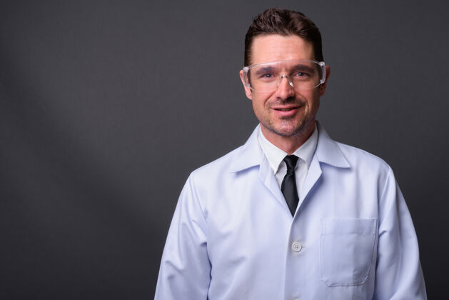 英俊英俊的大胡子男人 医生 科学家 戴着防护眼镜 挡在灰色的墙上医生胡须肖像