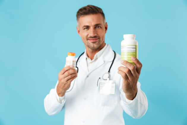 药片一幅欢快的医学专家的画像 身穿白大褂 手里拿着几罐药 孤零零地站在蓝色的墙上专家药片成熟
