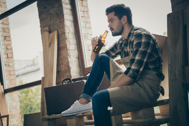 休息低矮的视角下 严肃自信的沉思的男人从瓶子里喝着啤酒 沉思地思考着他的下一道菜木工车间建筑工人
