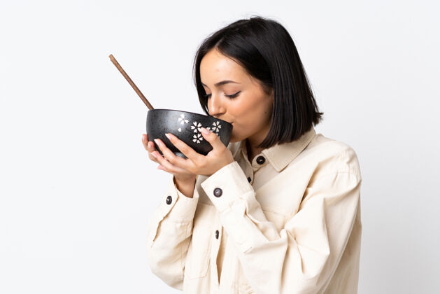 年轻年轻的白人妇女孤立在白墙上拿着一碗面条和筷子吃墙壁姿势黑发