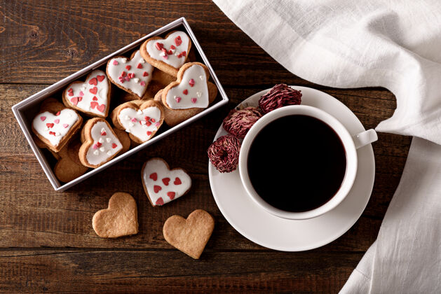 食物咖啡杯顶视图 棕色木质背景上有一盒心形饼干糖粉粉玫瑰
