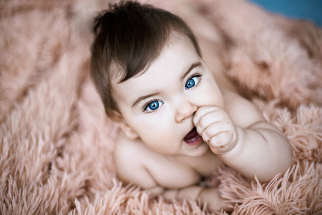 人美丽的蓝眼睛婴儿蓬松的浅橙色毯子 第一个牙齿的概念女孩美丽新生儿