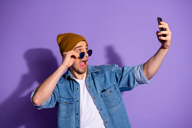 帽子照片中 帅哥手持电话 双手自拍 头戴棕色帽子 背景为鲜艳的紫色自我酷年轻
