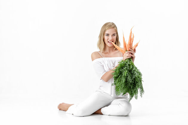 自然一个穿着白衬衫的金发美女 手里拿着一根新鲜的胡萝卜 上面有绿叶背景.健康还有节食健康女人营养