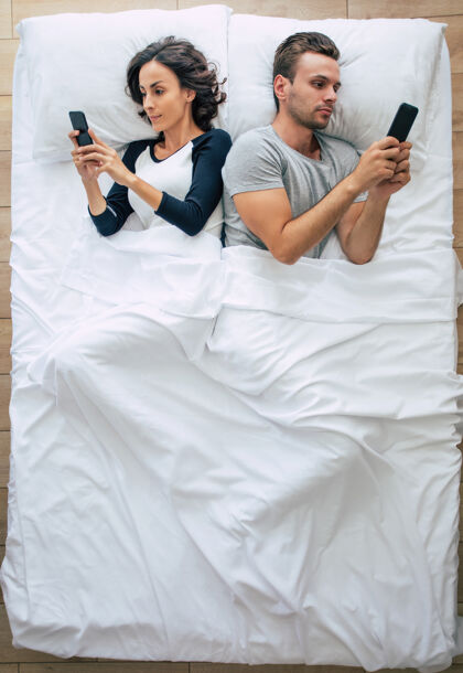 手机美女和帅哥躺在白色大沙发上用智能手机拍照床上聊天在线上面是这对夫妇的照片忽略男人电话