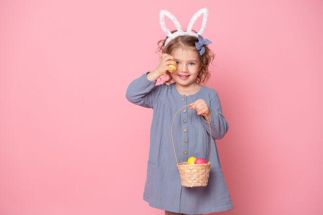 可爱有趣的小女孩在复活节兔子耳朵举行篮子彩色彩蛋粉红色复活节庆祝绘画