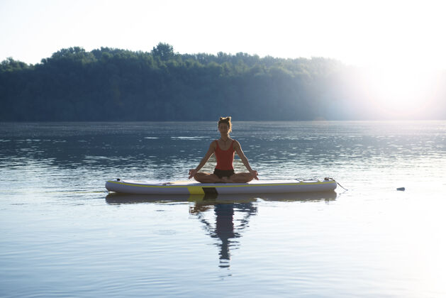 湖日出时坐在桨板上冥想的女人哈他活力夏天