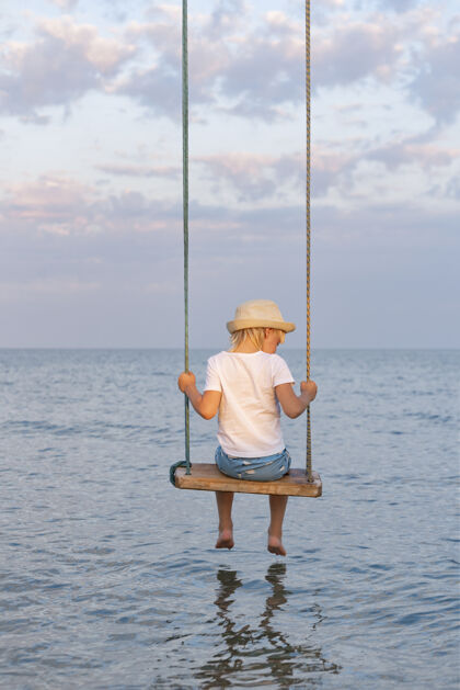 度假村男孩坐在绳子上荡秋千水秋千在沙滩上海洋青年水平