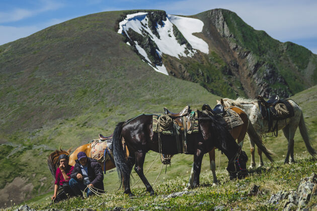草俄罗斯阿尔泰共和国乌拉甘斯基地区 年轻人和老骑手在山腰上走着三匹马自然马高地人