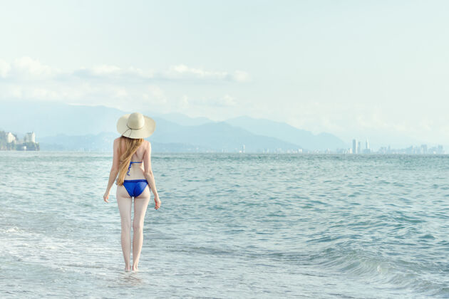 晒黑穿泳衣戴帽子的女人走过海景从后面格鲁吉亚女孩蓝色
