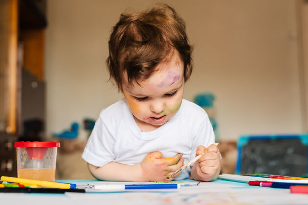 色彩一个可爱的小男孩用刷子和彩色颜料在一张纸上画画男孩发展休闲