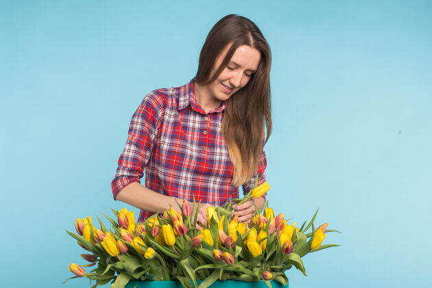 花店年轻的女花匠 蓝色表面上有一大盒黄色郁金香魅力花园职业