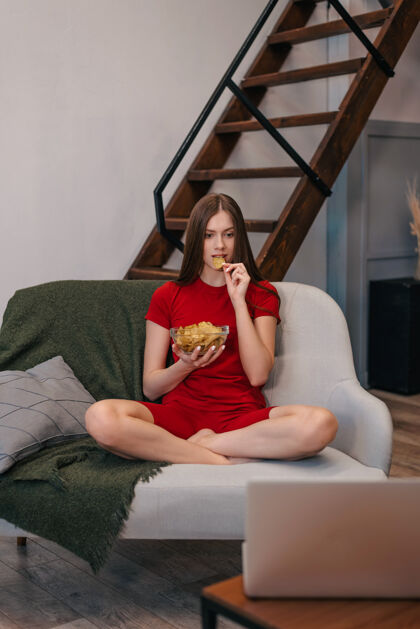 娱乐漂亮的家庭女孩吃薯片 看电视 坐在沙发上家庭坐着真诚