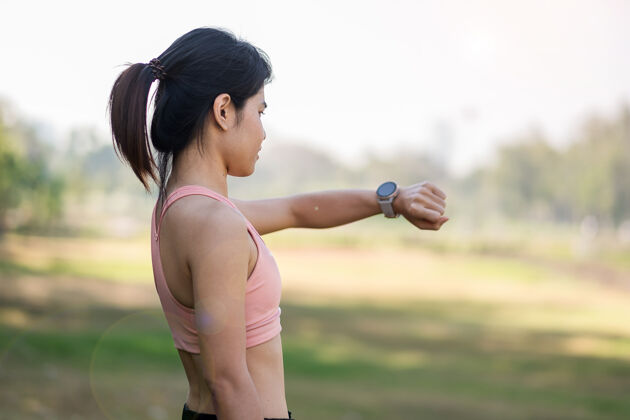 健康年轻成年女性在公园户外跑步时在sportsmartwatch上检查时间和有氧心率 跑步女性在公园慢跑晨练 科技 生活方式和锻炼检查健身训练