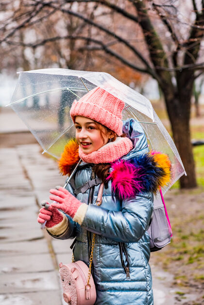 女孩金发碧眼的女孩穿着夹克带着透明的雨伞在外面的雨中御寒户外雨外套