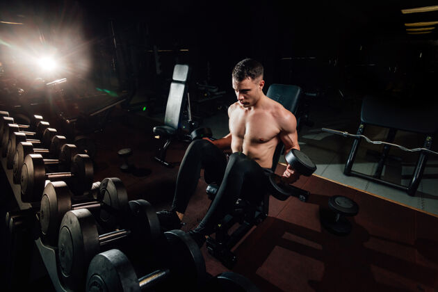 重量帅气的肌肉男 站在黑暗的现代体育馆里 用沉重的哑铃锻炼身体闪光强壮运动