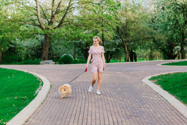 狗迷人的年轻女子抱着狗斯皮茨在外面 微笑着 走在街上公园概念关于人与动物之间的友谊收养快乐肖像