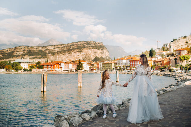海岸意大利 莱克加尔达时尚母女俩在意大利加尔达湖畔的山脚下阿尔卑斯山母亲女儿在意大利阿尔卑斯山户外孩子