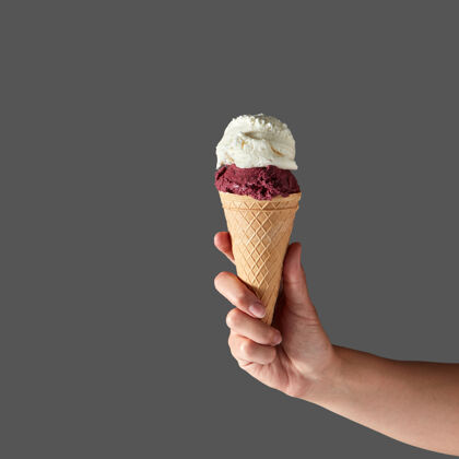 美食红色水果冰淇淋和牛奶冰淇淋 呈圆球状 放在华夫饼筒里 由一个女人的手放在灰色的桌子上墙.夏季复制空间概念甜点牛奶冷冻