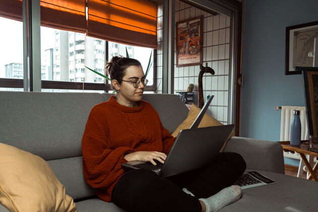 教师一个戴眼镜的年轻女子在一个现代家庭的沙发上用笔记本电脑工作和学习笔记本电脑年轻室内