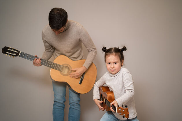 音乐家爸爸用手弹吉他女儿孩子学会用钢琴演奏乐器音乐导师父亲和孩子的二重唱在一起音乐家庭