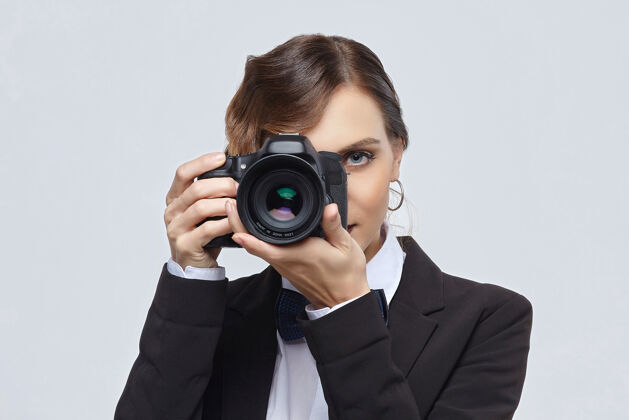 年轻美丽的女摄影师在一个男人的西装和复古发型的白色背景相机人物领结