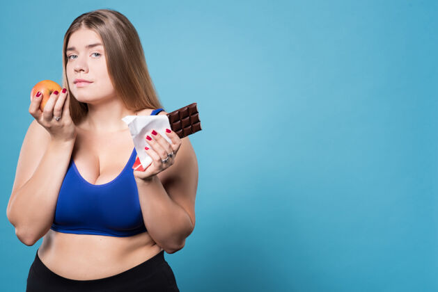 饮食两种方法生活肖像年轻漂亮的胖女人站在苹果和巧克力旁边身材巧克力半身