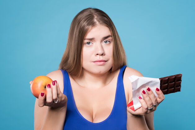 素食主义者做什么选择关闭一个抱着苹果和巧克力的漂亮的胖女孩微笑丰满女性