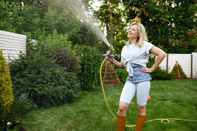 苗圃微笑的女人拿着水管在花园里给树浇水花园女园丁照顾植物户外 园艺爱好 花店的生活方式和休闲浇水活动人