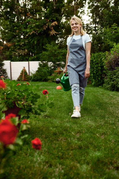 苗圃围裙上戴手套的女人手里拿着水罐花园女园丁照顾户外植物 园艺爱好 花匠的生活方式人活动人